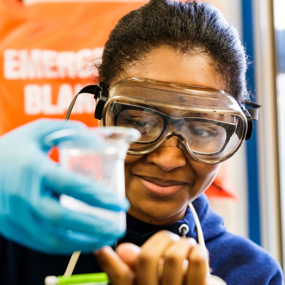  An early college student holds a beaker while wearing safety goggles