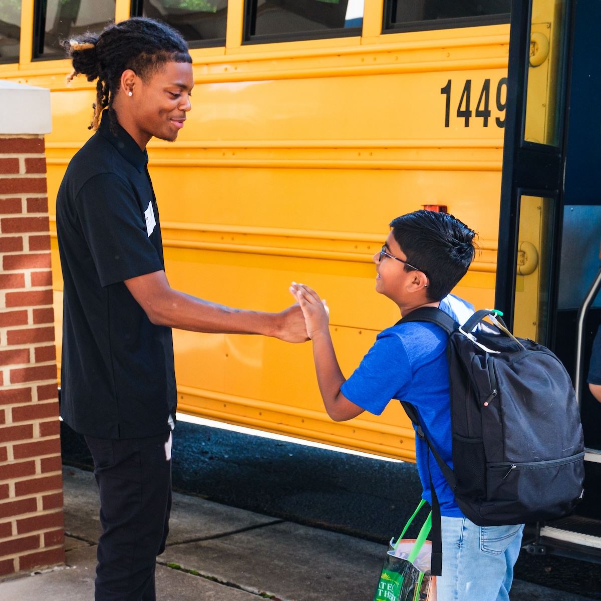  A school volunteer fist bumping a student getting off the bus