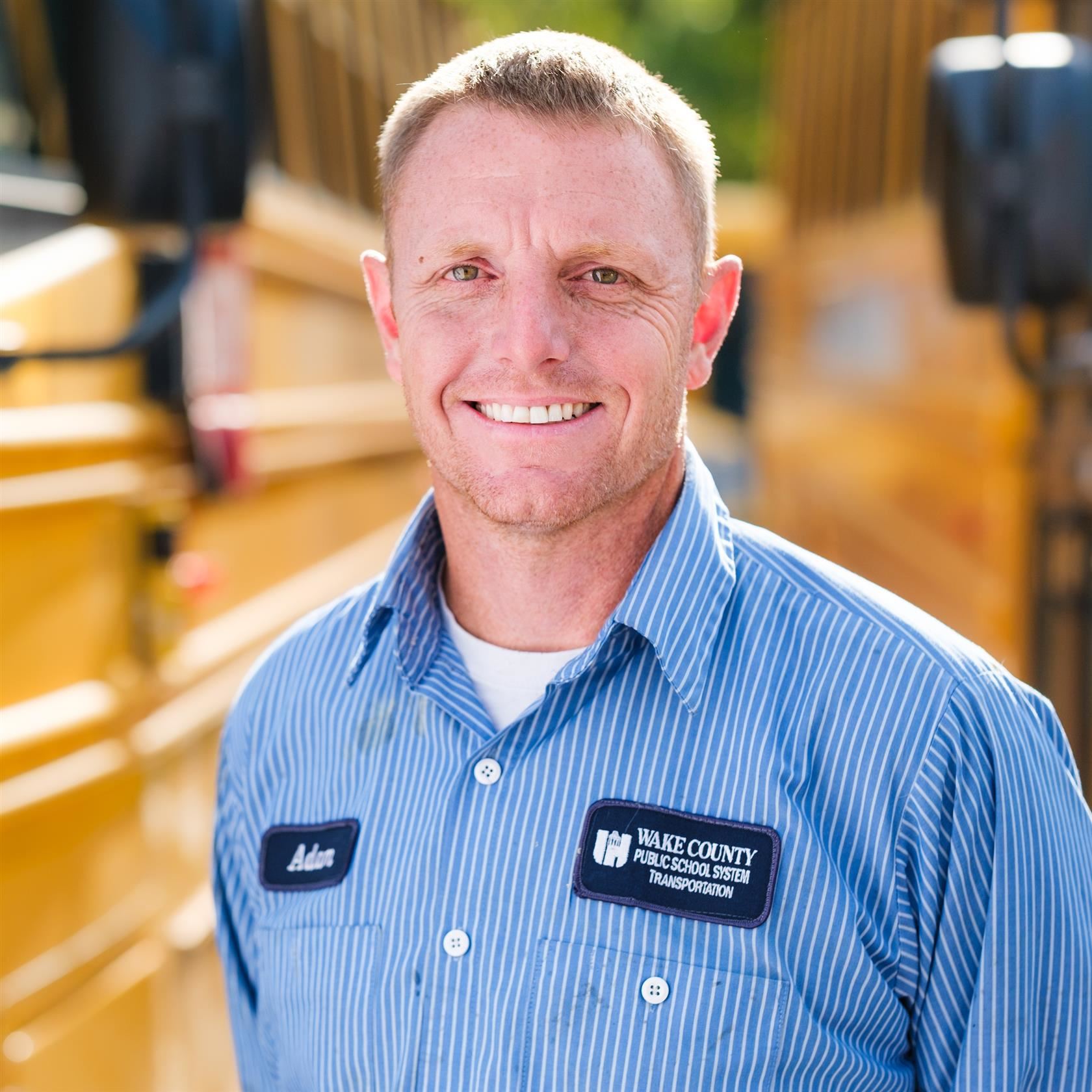  A school bus mechanic smiles in front of a yellow bus