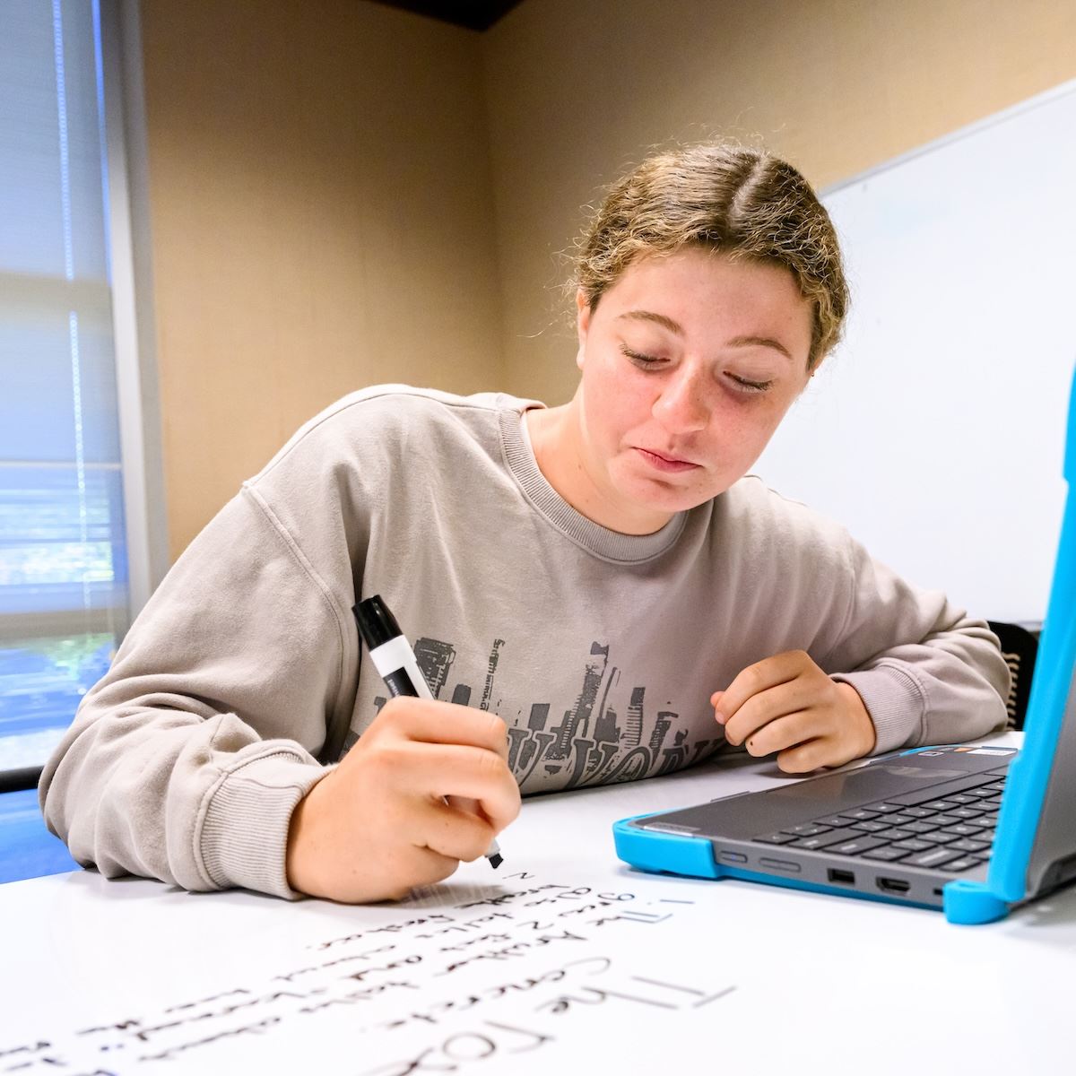  A student writes with a marker next to an open laptop