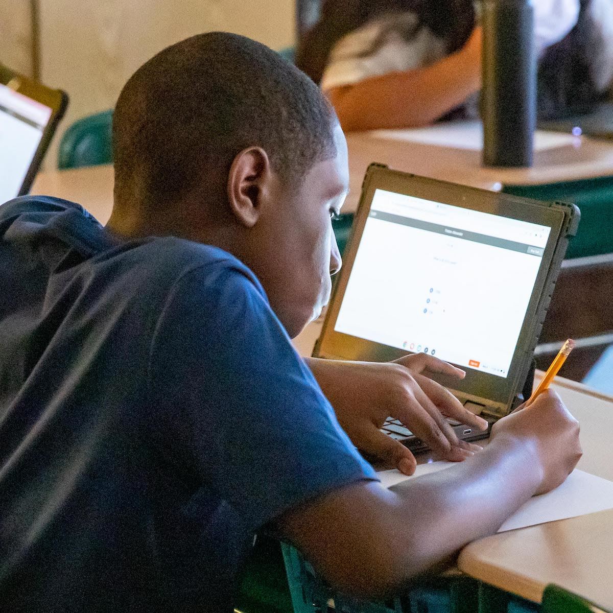  A student writes at his desk with a laptop open