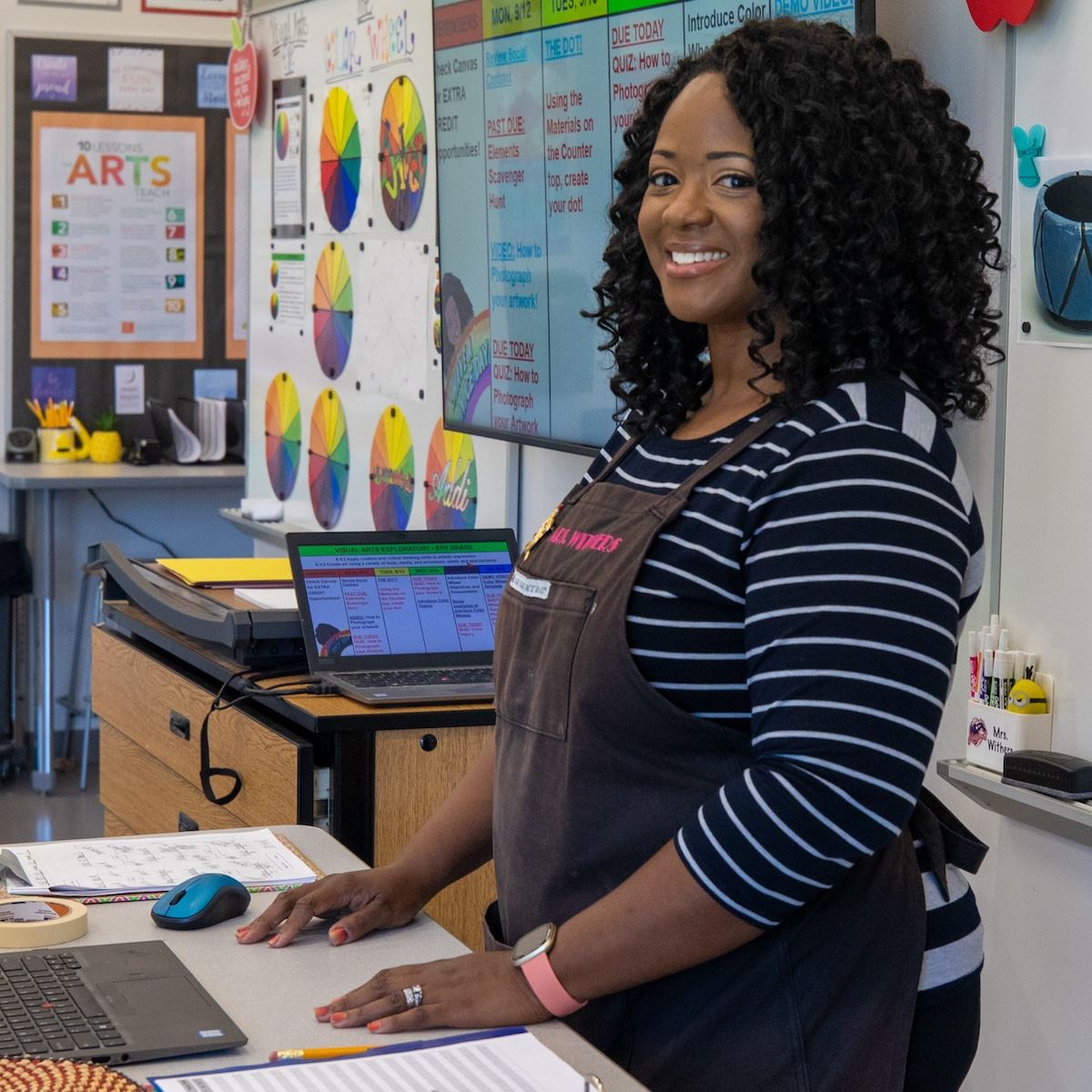  A middle school art teacher smiles while standing in front of student projects on the wall