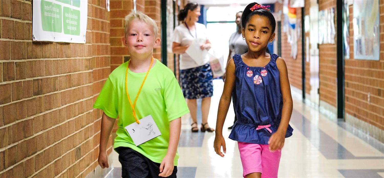 Elementary students are walking down a school hallway 