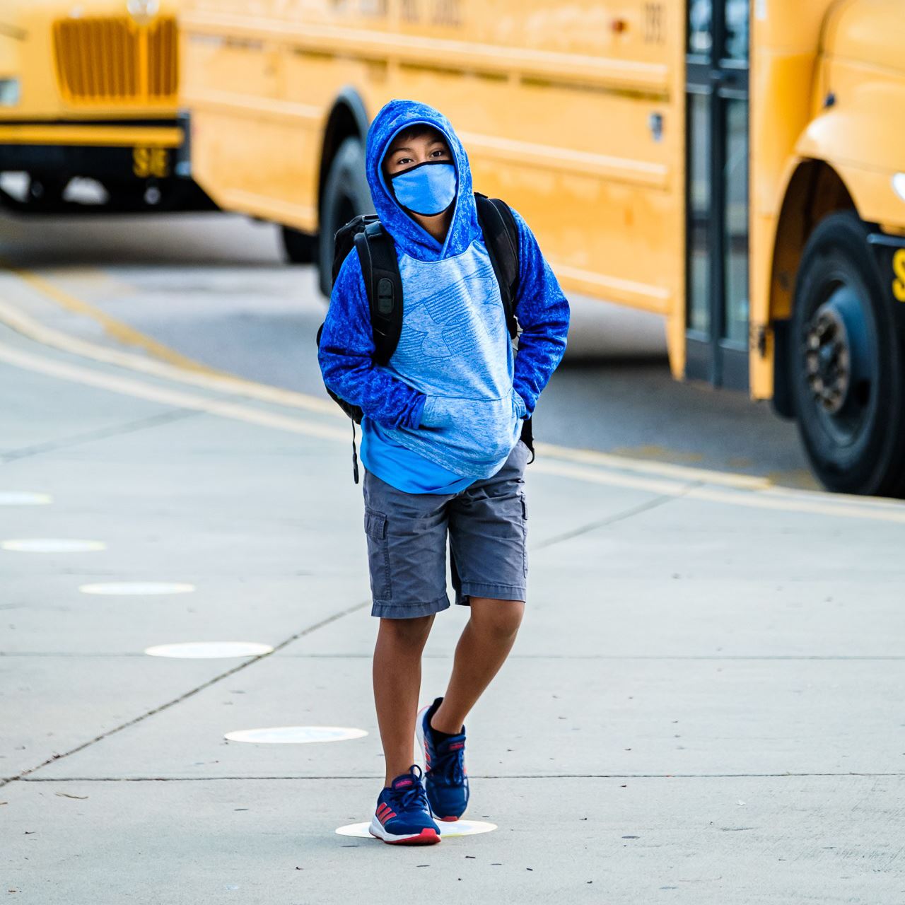  boy wearing a face covering walking away from a bus