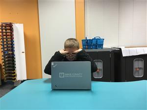 picture of young boy at a laptop making eye glasses with his hands 