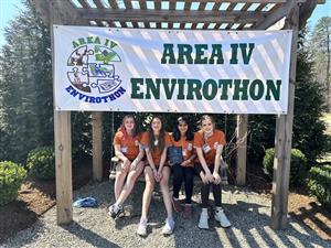 Four students sitting on a porch swing under an Area 4 Envirothon poster