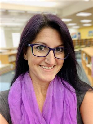 Headshot  of white woman wearing glasses and a purple scarf in a library